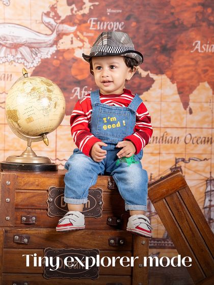 Tiny explorer mode is on! This little adventurer is ready to plan his next trip, dressed in overalls and a hat, surrounded by maps and luggage.
