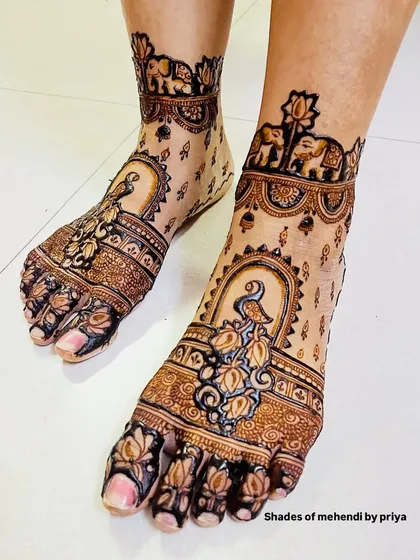 This foot mehendi design features peacocks in a jharokha, with delicate lotus and elephant details on the ankle band.