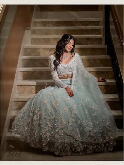 An elegant seated portrait of the bride on the stairs, her voluminous lehenga spread out around her. This classic pose creates a regal and timeless bridal image.