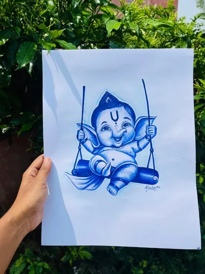 The finished blue pen sketch of baby Ganesha on a swing, held up outdoors. The natural background makes the blue ink pop.