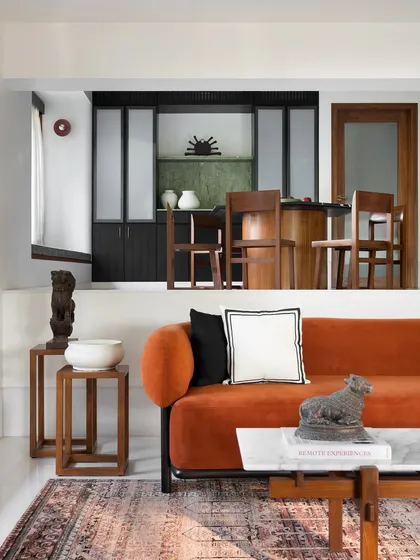 I designed the furniture for this split-level home to enhance the unique architecture. The custom orange sofa provides a grounding focal point in the living area, while the wooden side tables add warmth and complement the view into the raised dining space.