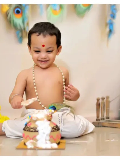 A happy baby enjoying his 'dahi handi' cake during a Krishna-themed cake smash. This is a fun and unique way to celebrate a first birthday.