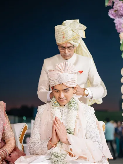 A father adjusts his son's turban, a quiet moment of blessing and pride before the wedding ceremony begins.