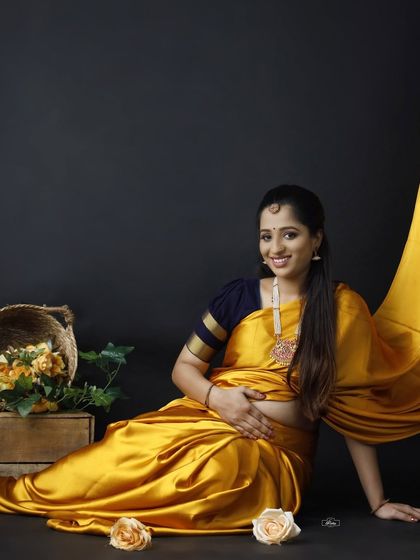 A lovely seated portrait of a mother-to-be in a vibrant yellow saree. The use of floral props adds a soft, natural touch to this classic studio setup.