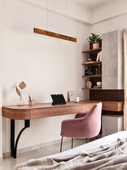 This elegant study nook features a floating wooden desk with a beautiful curved edge, supported by stylish black metal brackets. The combination of a pink upholstered chair and concrete-finish shelving creates a modern and sophisticated workspace.