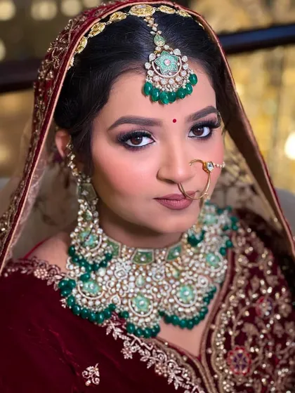 A close-up showcasing dramatic eye makeup. This look features a dark smokey eye with a sharp wing, paired with a matte mauve lip and stunning oversized emerald jewelry.