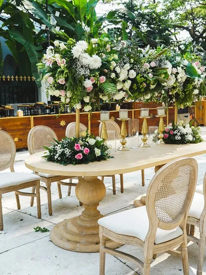 An elegant dining setup featuring a classic wooden table and tall floral centerpieces. The combination of white and pink flowers with lush greenery creates a timeless and romantic look.
