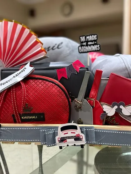 A vibrant red and grey themed hamper for a newlywed couple, celebrating "The Magic of New Beginnings". This gift includes personalized caps, matching pouches, and travel accessories for their journey ahead.
