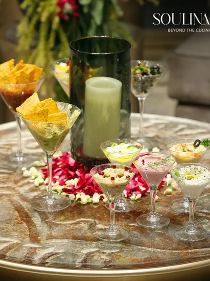 A beautiful centerpiece of assorted dips and chips in martini glasses, surrounded by flower petals. A simple yet elegant touch for any table.