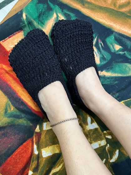 A pair of handmade black crochet socks, perfect for lounging at home. These ankle-length socks are warm and comfortable.