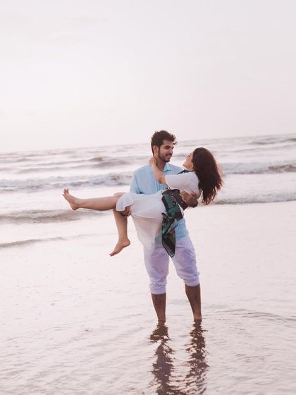 A classic romantic pose, with him carrying her in the shallow waves. This pre-wedding beach photo feels both heroic and tender.