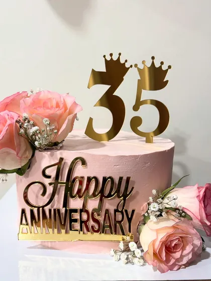 A one-kg anniversary cake in a soft pink, decorated with fresh roses, baby's breath, and a golden "Happy Anniversary" topper.