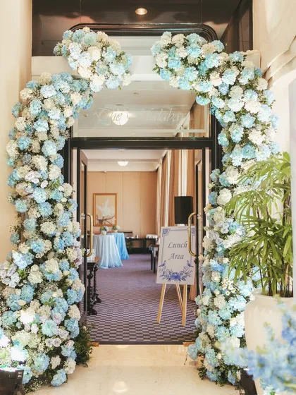 The grand entrance to the lunch area, framed by a lush arch of blue and white flowers, inviting guests into the beautifully styled space.