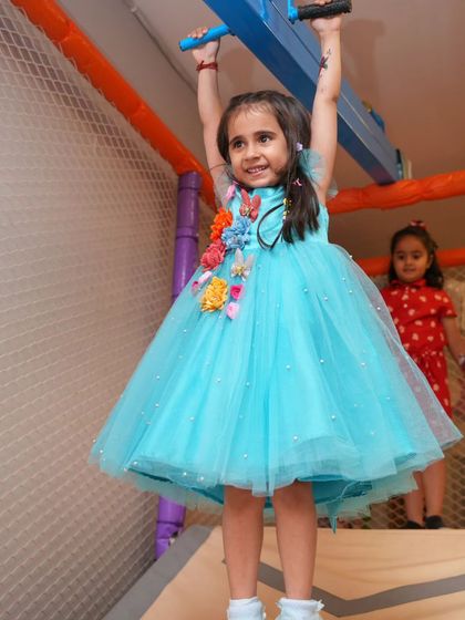 Strong and smiling! A little girl shows off her strength on the monkey bars in our soft play area, dressed like a princess.