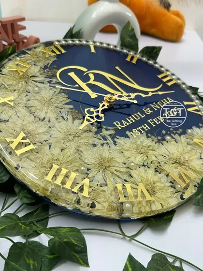 A close-up shot focusing on the intricate details of the preserved white flowers and the elegant clock hands over the couple's names.
