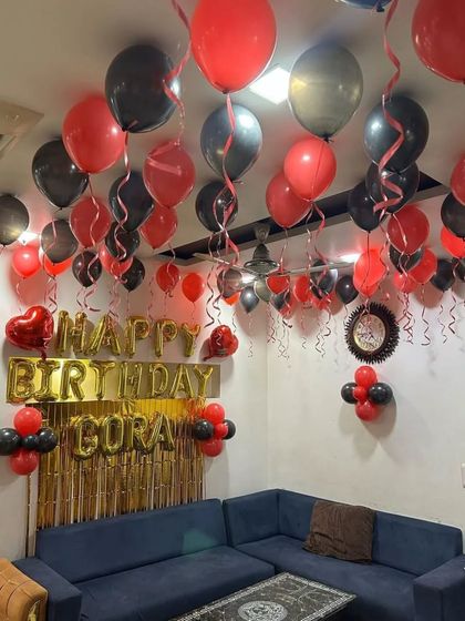 A living room decorated with red and black balloons on the ceiling, a gold fringe backdrop, and personalized name balloons.