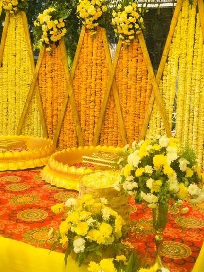 A traditional Haldi seating area with a backdrop of triangular panels covered in marigold flowers.