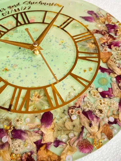 A close-up of a 12-inch clock made with preserved orchids. The light green resin and gold details create a fresh and elegant look.