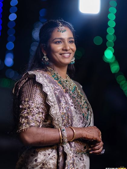 A happy, smiling shot of Sruthi against a bokeh background. Her glamorous makeup looks stunning, and her joy is palpable.