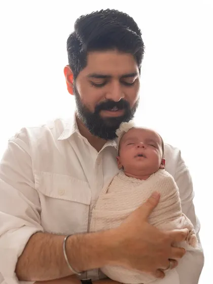 A proud father holds his sleeping newborn daughter close to his chest. The white-on-white styling creates a timeless and classic portrait.