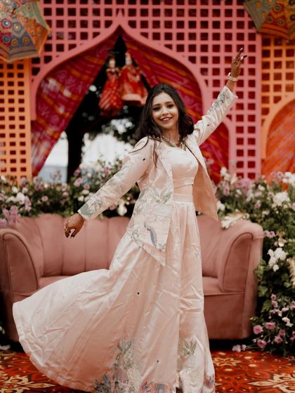 The bride in a joyful, dancing pose at her Sangeet, with colorful decor in the background.