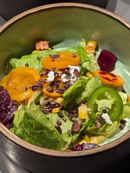 A refreshing salad with fresh greens, beets, corn, and a sprinkle of cacao nibs. The nibs add a delightful crunch and a slightly bitter, earthy note that balances the sweetness of the other ingredients.