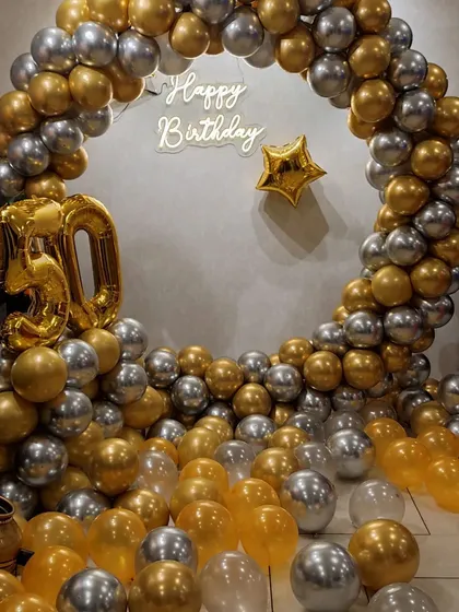 Celebrating a 50th birthday in style with this sophisticated gold and silver balloon arrangement. The decor features a full ring of metallic balloons, a "Happy Birthday" neon sign, and large gold foil number balloons for the age. The floor is filled with loose balloons to create an immersive, celebratory feel.