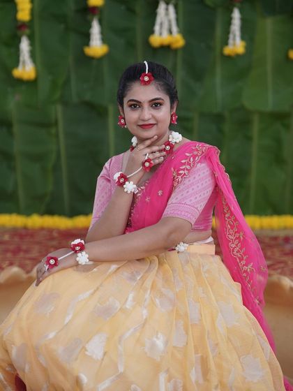 A bride looking lovely at her Haldi ceremony, wearing custom floral jewelry made of red and white flowers that complements her outfit.