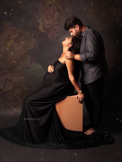 An intimate and loving pose where the father-to-be gently kisses his partner's forehead. The dramatic lighting and the elegant black gown create a timeless and romantic maternity photograph.