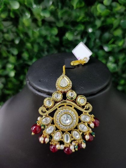 A classic round kundan maang tikka with red bead drops, a timeless choice for any bride.