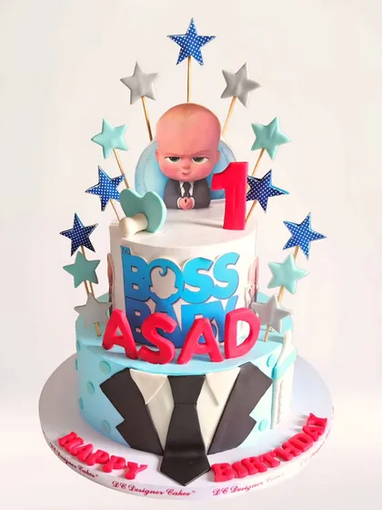 A two-tier Boss Baby cake for a first birthday. This fun whipped cream cake features the iconic suit and tie on the bottom tier and the Boss Baby himself on top, surrounded by stars.