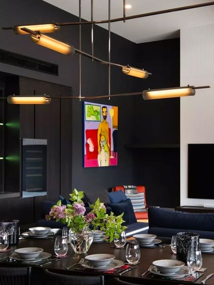 The Volant chandelier provides elegant lighting over a dining table in a dark, moody interior, its warm brass tones complementing the rich color palette.