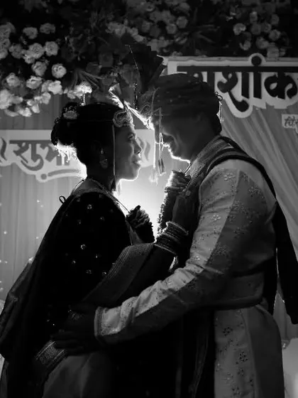 Even in the middle of a ceremony, we look for cinematic angles. This black and white shot captures the couple in a tender moment, backlit by the stage lights to create a soft glow and silhouette effect against the wedding decor.