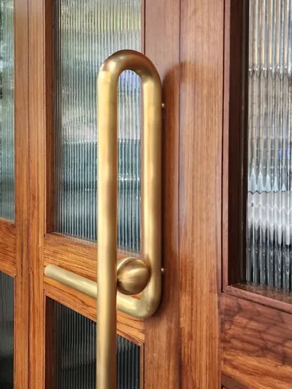 A close-up of the custom brass door handle for Americano. The elongated, curved form is a unique sculptural element that makes a statement at the restaurant's entrance.