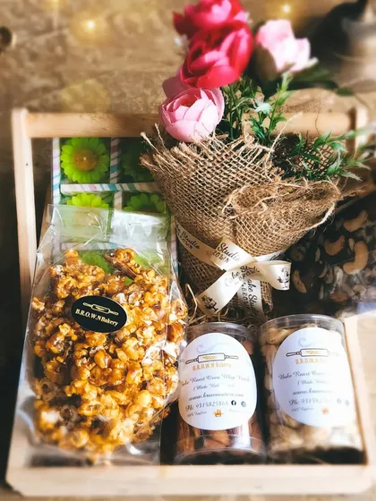 Our Floral Indulgence Wooden Gourmet Hamper is a feast for the senses. It combines sweet and savory snacks like caramel popcorn and roasted nuts with a beautiful floral bouquet, all packed in a reusable wooden tray.