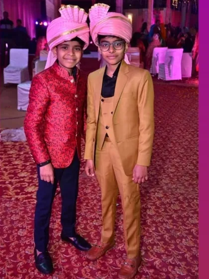 Custom ethnic wear isn't just for adults. Here are two young clients looking smart in their tailored outfits, a red brocade Jodhpuri jacket and a tan three-piece suit, for a family wedding.
