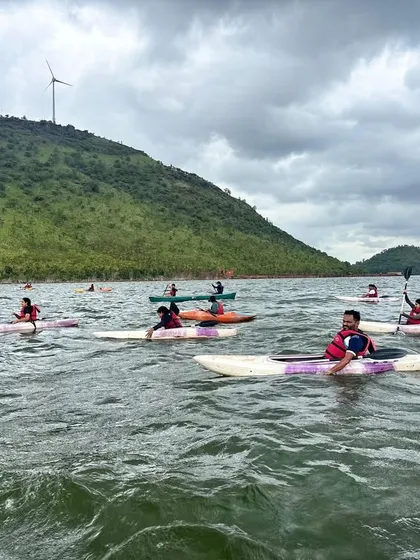 A group of kayakers spreads out across the water at Vani Vilas Sagar, enjoying the freedom and scenery. You can see the windmills on the surrounding hills, a unique feature of this location.