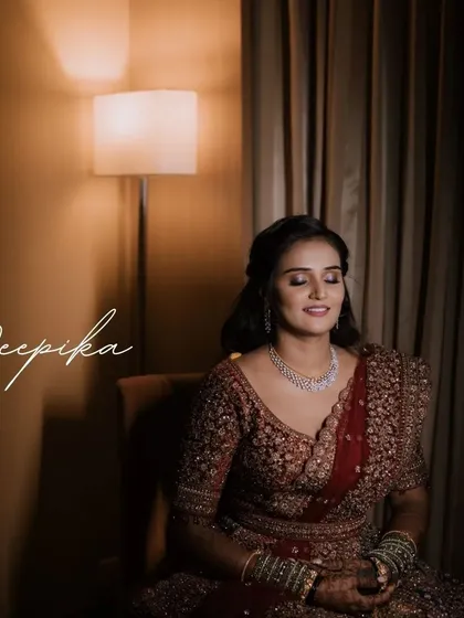 A serene bridal portrait in a warmly lit room. The bride's rich, embroidered lehenga and her peaceful expression create a moment of quiet elegance.