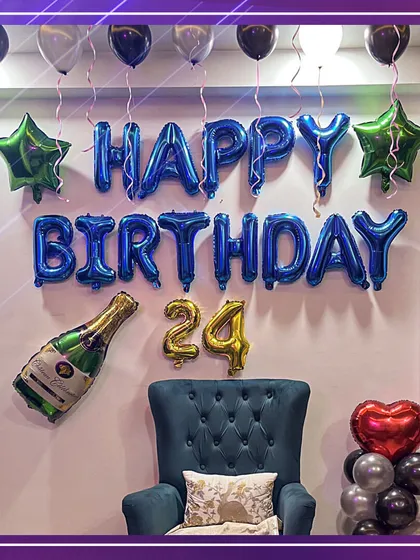 Cheers to 24 years! A simple yet stylish birthday setup for him, featuring 'HAPPY BIRTHDAY' foil letters in bold blue, a champagne bottle balloon, and a comfy chair for the birthday boy to feel like a king.