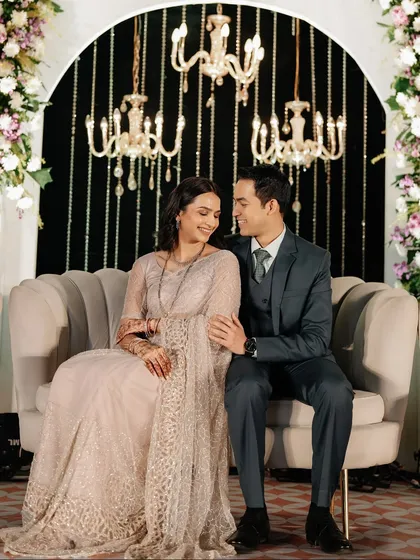 Seated on their reception stage, under the warm glow of chandeliers, the couple shares a look of pure happiness. We designed the stage to be both grand and intimate.