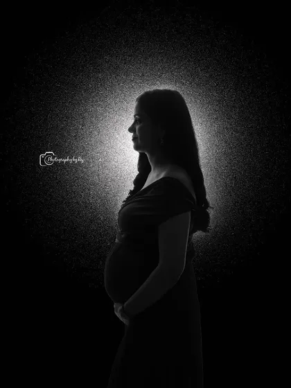 A dramatic rim-lit silhouette portrait, creating a halo effect that beautifully outlines the mother-to-be's form.