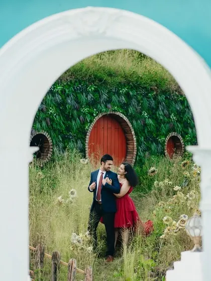A whimsical shot of the couple framed by a white archway, with a Hobbit-hole-like structure in the background. This unique location adds a touch of fantasy and fun to their pre-wedding album.