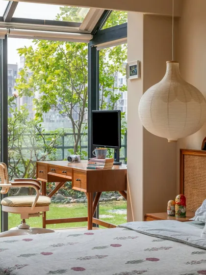 A study desk is placed by the window in this Calcutta bedroom, creating a perfect spot for reflection with a view of the garden. The mix of a vintage-style desk, a modern paper lantern, and patterned bedding gives the room a collected, eclectic feel.
