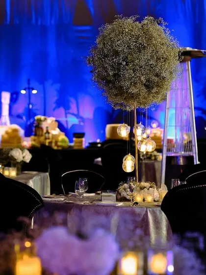 A dining table centerpiece featuring a tall, spherical arrangement of baby's breath, creating a modern and elegant look against the deep blue backdrop.