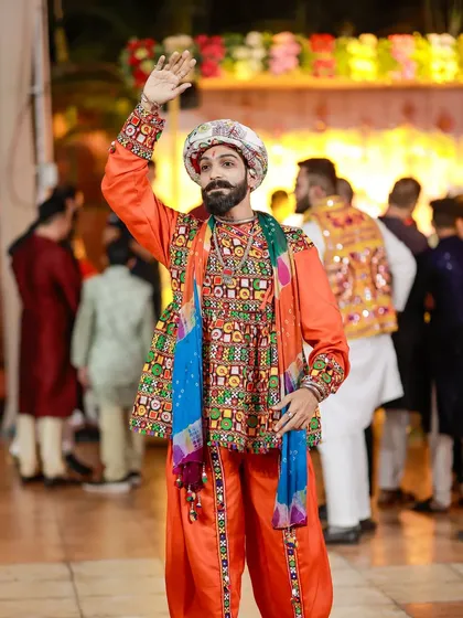 A male dancer in a vibrant orange and embroidered costume waves to the crowd, fully embodying the festive spirit.