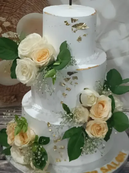 An elegant three-tiered wedding cake with a unique offset design. It's adorned with delicate fresh-looking sugar roses and baby's breath, with a touch of edible gold leaf for a hint of luxury.