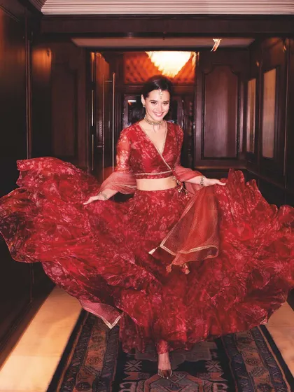 Capturing the festive spirit for a Biba campaign, this shot uses a voluminous red printed lehenga. The styling creates a sense of joyful celebration through the twirling motion, which highlights the flow and flare of the fabric in a dynamic hotel corridor setting.