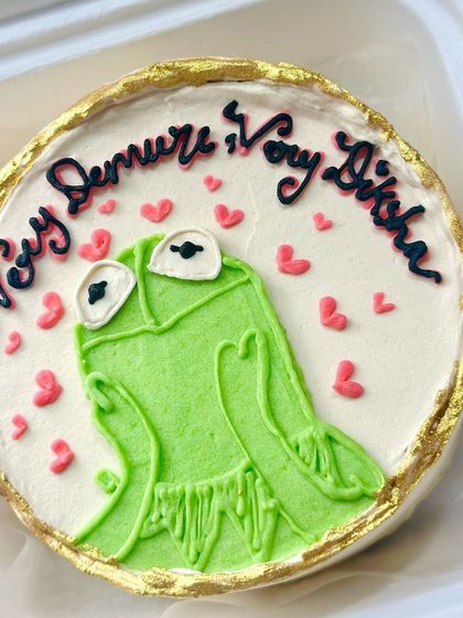 A Kermit the Frog bento cake with a funny, trending phrase. We use edible gold leaf to add a touch of glam to this playful, hand-piped character.