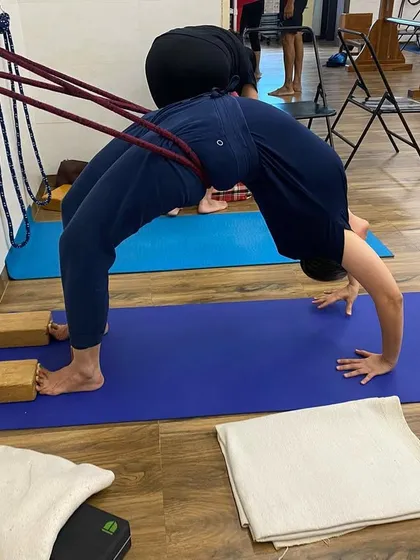 Using the wall ropes for support in Urdhva Dhanurasana (Upward Bow Pose). The ropes help to open the shoulders and lift the dorsal spine, making the backbend deeper and safer. This is an advanced backbend practice.