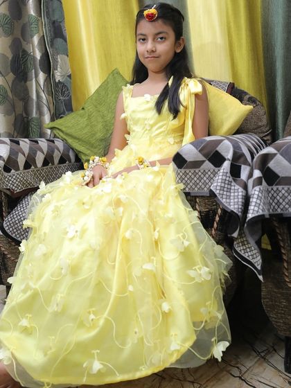 A full-length view of the adorable yellow gown for kids, complete with a small floral maang tikka.